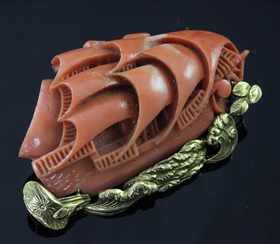 A Chinese 14ct gold mounted carved coral brooch, modelled as a masted ship at sea, 2.25in.